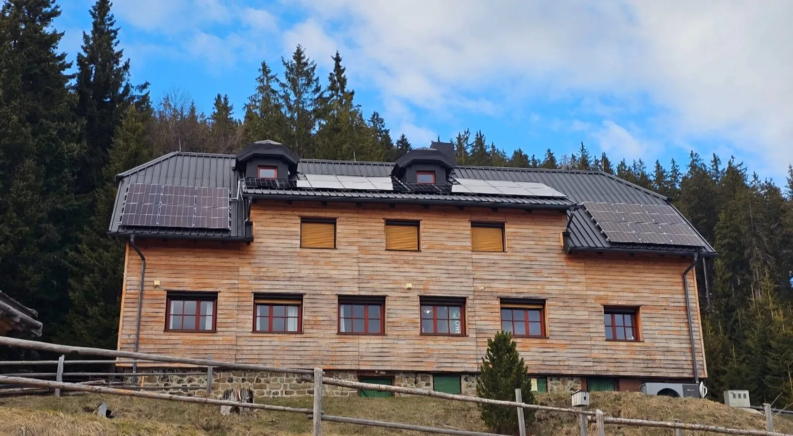 Dom na Smrekovcu z lesenim pročeljem in gozdnim ozadjem